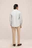 Back view of man in light blue linen shirt with apple-cut hem and soft drape, paired with beige pants and loafers.
