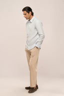Man wearing linen shirt in light blue featuring full sleeves and relaxed fit, side profile with beige pants and loafers.
