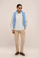 Man wearing linen shirt for men in light blue with relaxed fit and curved hem, styled with beige pants and blue sweater.