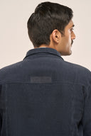 Close-up of man wearing navy corduroy jacket showing TZÁR logo back detail and ribbed texture.