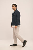 Man walks in profile wearing navy corduroy jacket, white shirt, beige pants, and black shoes against a plain background.