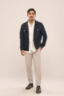 Man stands against plain background in navy corduroy jacket, white shirt, light pants, and black shoes.
