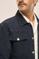Close-up of a man wearing a navy ribbed corduroy jacket with metal buttons, flap pockets, layered over a white shirt.