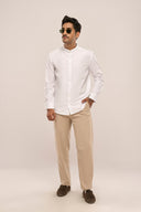 Man wearing white mandarin collar shirt with full sleeves and relaxed fit, paired with beige pants, loafers and sunglasses.