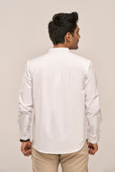 Back view of man wearing white mandarin collar shirt with loop-and-pleat yoke, full sleeves and relaxed fit, beige pants.